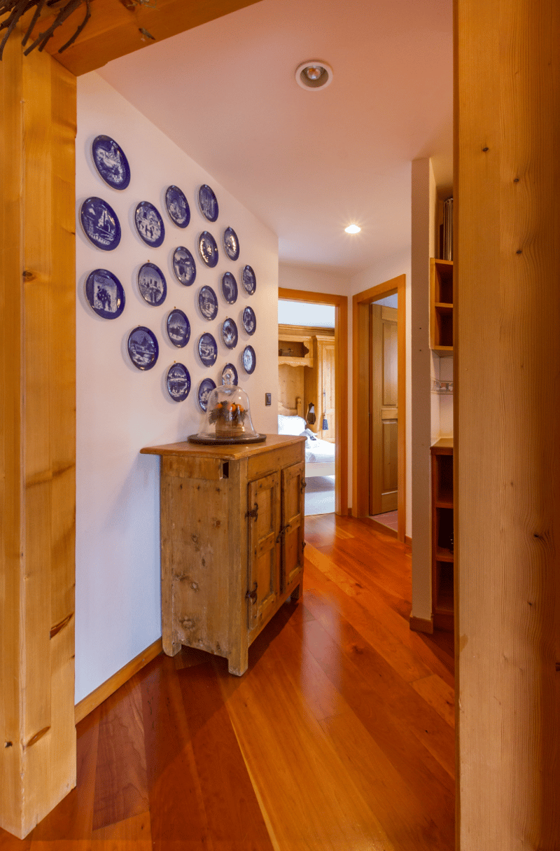 Wooden hallway, wood flooring, wall decorated with blue plates, wooden cupboard with glass cover, entrance to bedroom