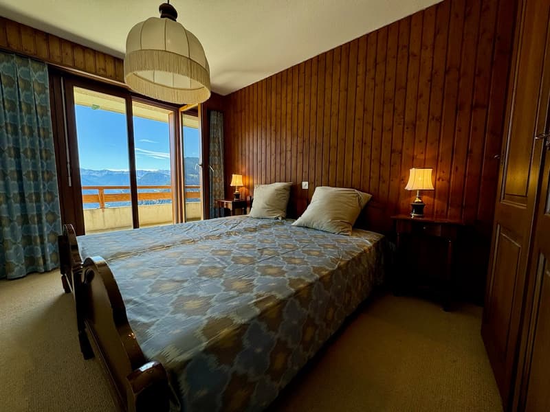 wooden wall, carpeted floor, wooden bed with bedspread, night lamps, windows, balcony