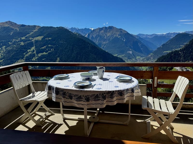 Terrace with two white folding chairs and a table with white tablecloth, a jug and plates set for meal