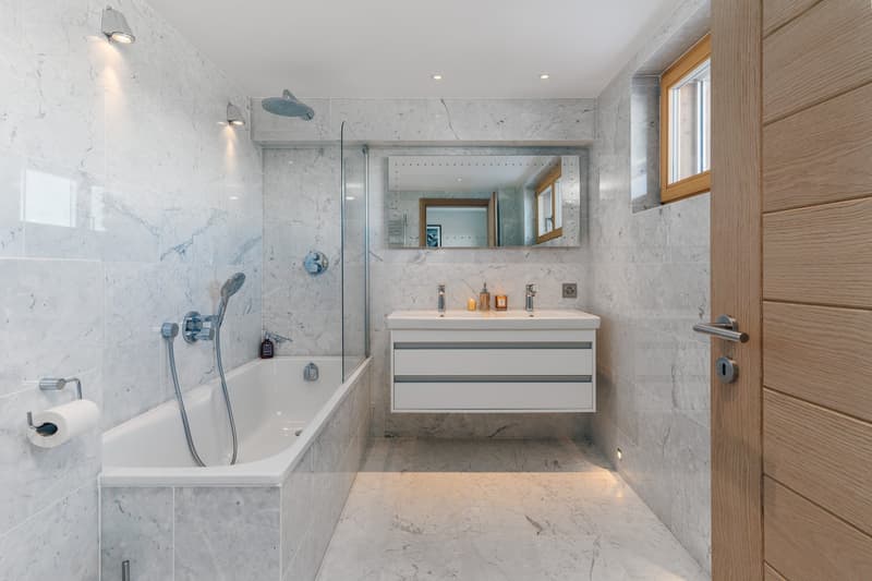 modern bathroom with white marble tiles, bathtub, glass shower enclosure, vanity with sink, mirror, and wooden door