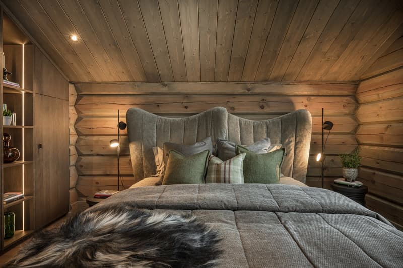 a cozy bedroom with wooden walls, a bed, nightstands, a wooden cabinet, a fur throw, and lamps