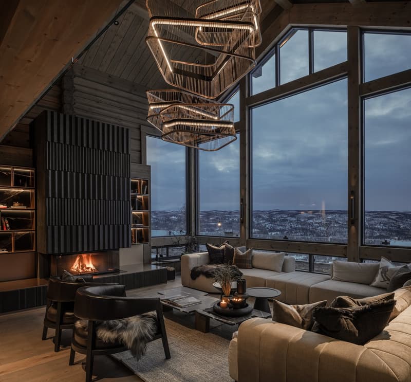 Large glass windows, fireplace, large couch, 2 armchairs, rug, center table, modern pendant light, wooden floor