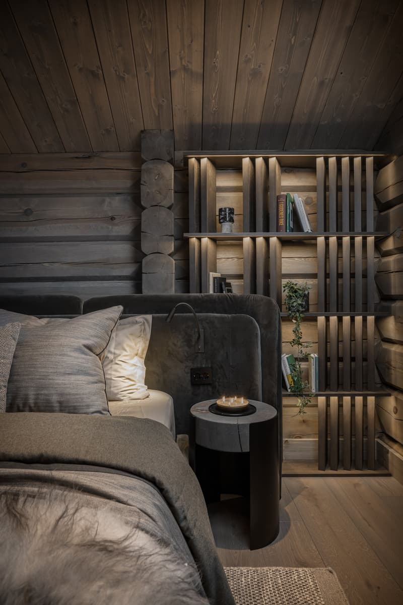 Bedroom with wooden walls, bed, lamps, nightstand, plant, and a wall-mounted shelf.