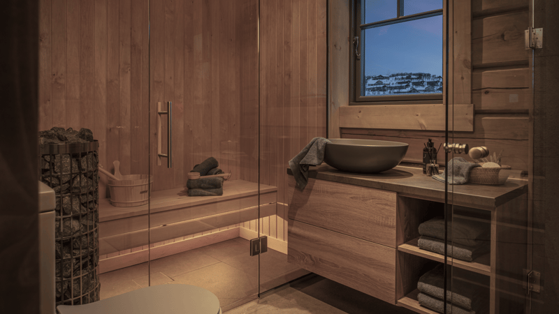 Interior with glass walls, wooden cabinets, a wooden sink with a towel, a wooden sauna bench, a bucket, towels, shampoo, and a view from the window