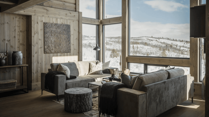Ample windows with a mountain view, gray couches, wooden round coffee table, floor to ceiling windows