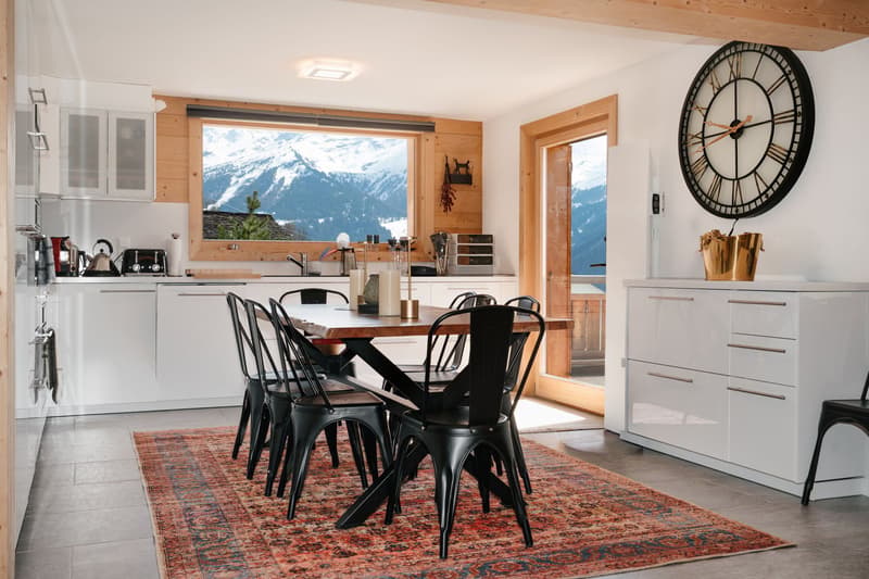 modern kitchen with dining area, wooden table, black chairs, white cabinets, large window with mountain view, wooden floor, large clock on wall