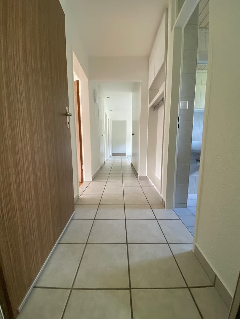 White tiled walls, wooden ceiling, rectangular window, shower area, white bathtub with ledges, white cabinet
