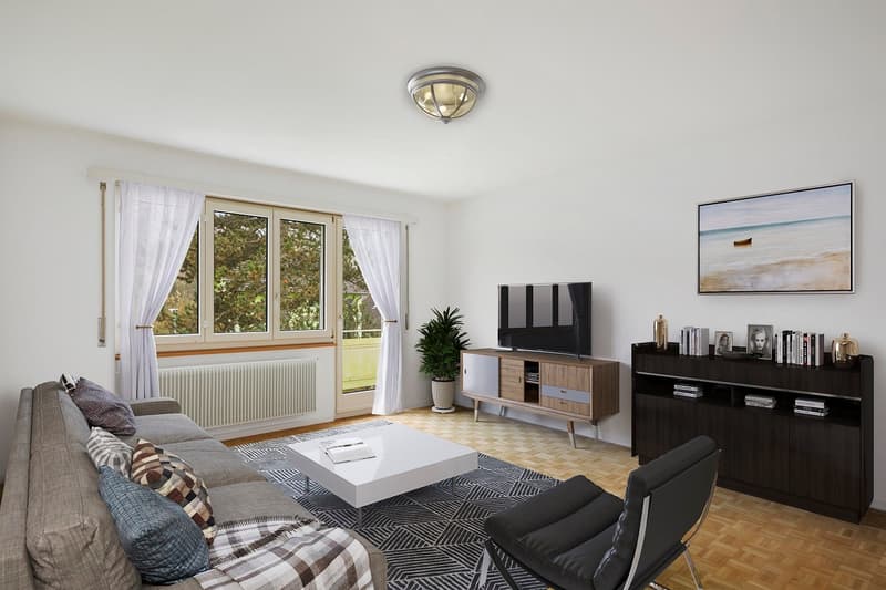 Spacious living room with large windows, white curtains, hardwood floors, gray sofa, coffee table, TV stand, and shelving unit. The room has a modern and minimalist design with a balcony or terrace visible through the windows.