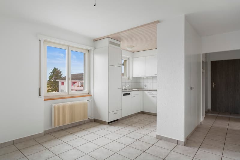 Empty kitchen with white tiles, white kitchen units, a sink, and a window.