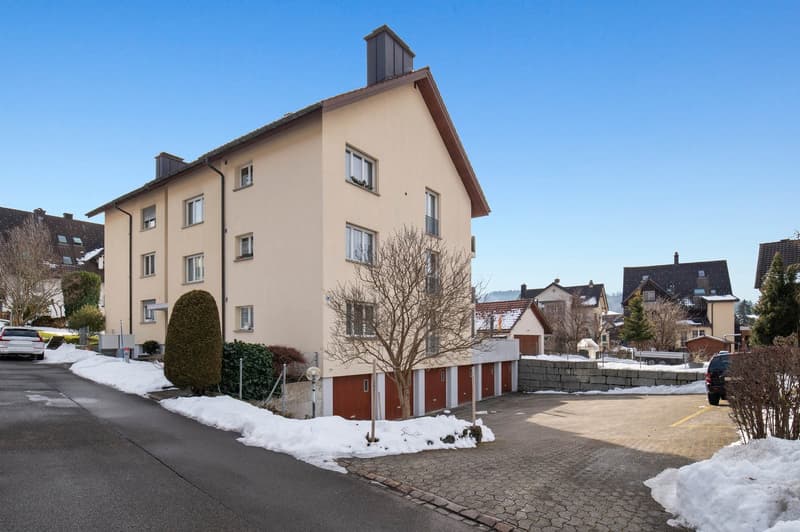3 story beige building, covered parking, covered pathway, small garden in front