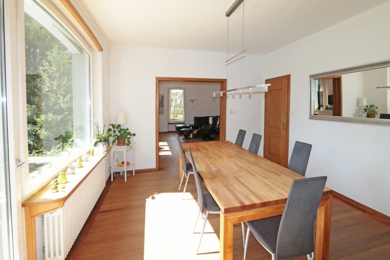 Essbereich als Verbindung zwischen Küche und Wohnen mit Ausgang in den Garten / a dining room with a long table and wooden chairs and a large window