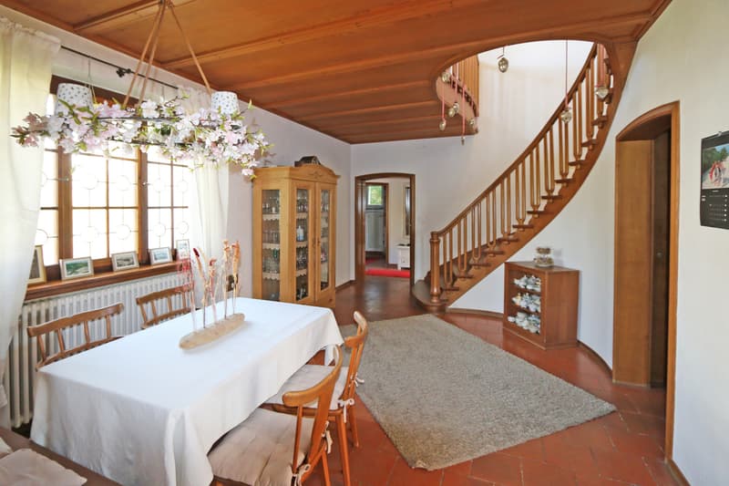 historische Halle mit Treppenaufgang / a dining room with a white table and chairs and a wooden staircase to the second floor