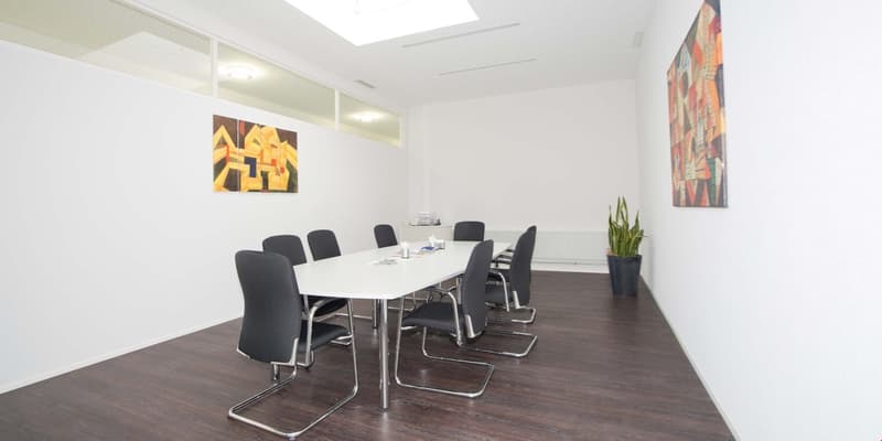 conference room, white walls, wooden floor, long white table, black chairs, two paintings, potted plant
