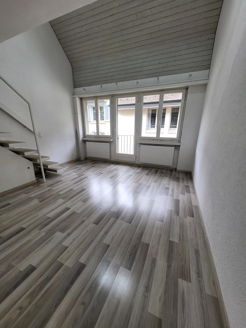 large room with wooden flooring and white walls, three windows, stairs leading to upper floor