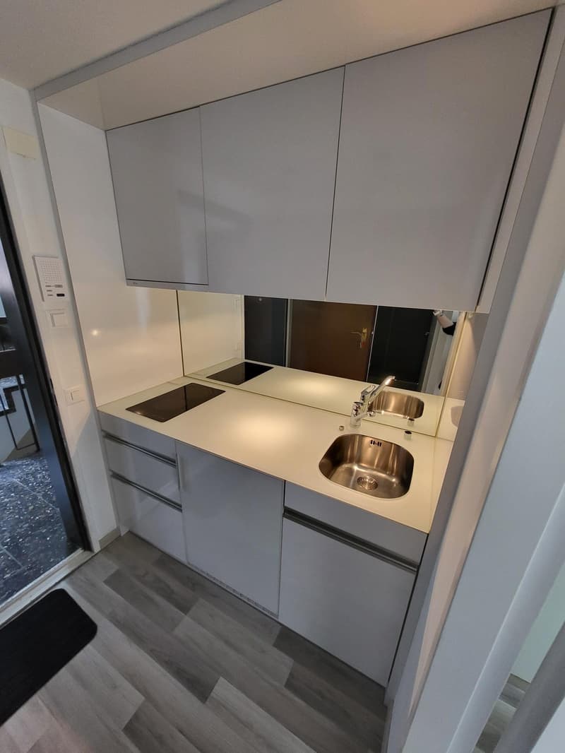 modern compact kitchen with a sink, gas stove, cabinets, a sliding door to a room, and a mirror on the wall