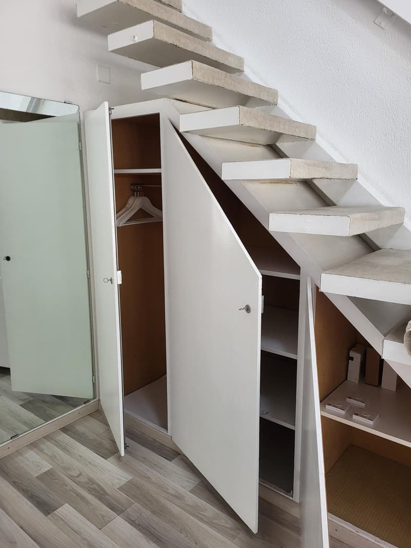 Storage under stairs, white shelves, open door, mirror, white hanger