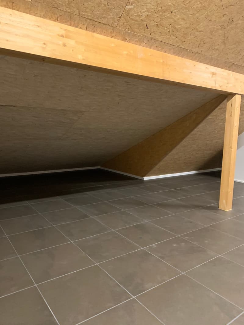 The image shows a room with a wooden ceiling and gray tile flooring. The room appears to be unfinished, with exposed wooden beams and a bare concrete floor. The space looks like it could be a basement or attic area that is being renovated or converted int