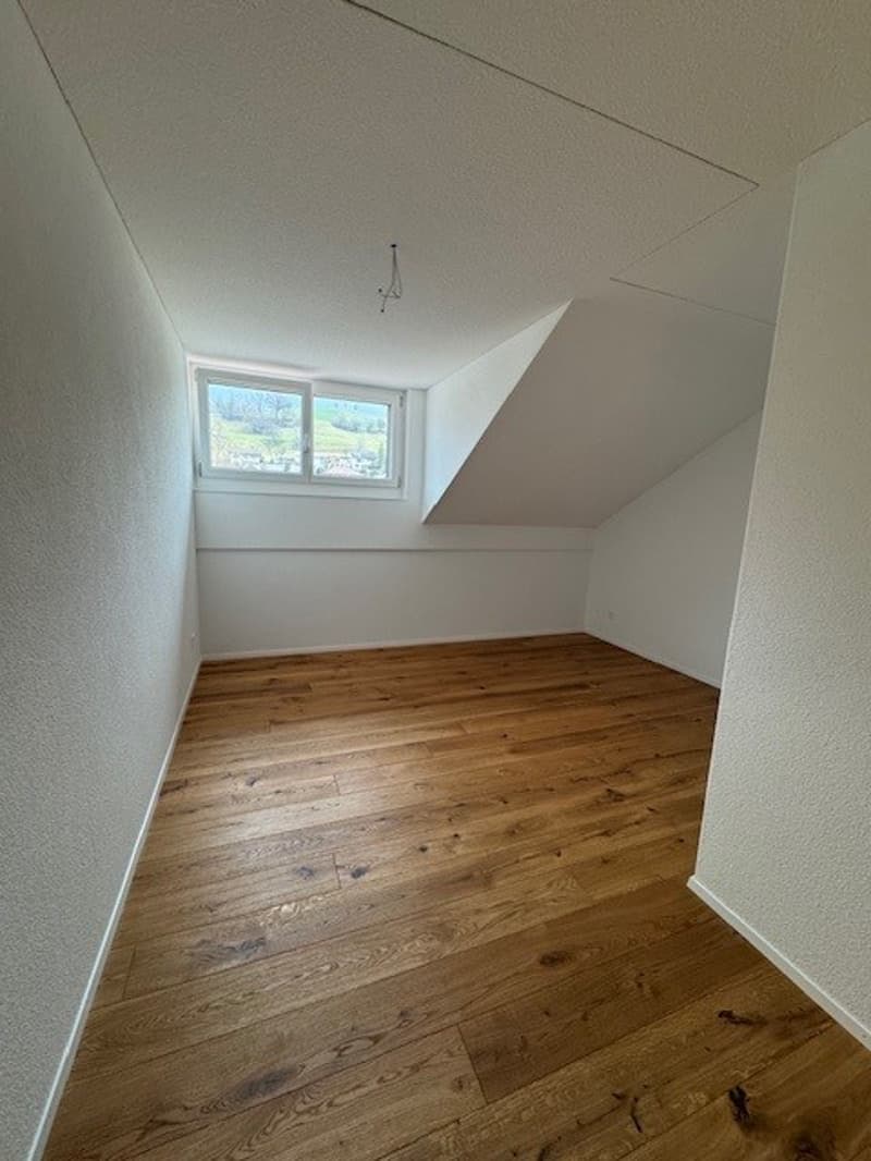 Empty room with wooden floor and white walls, small window on one wall