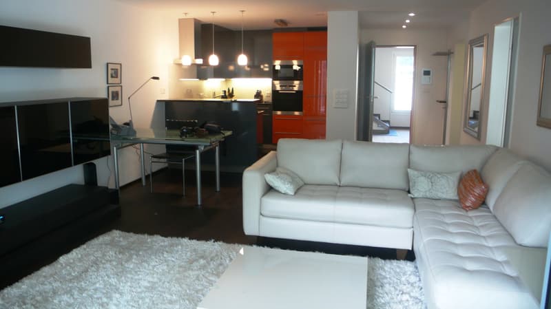 modern living room with white leather couch, dining table, black television cabinets, carpet, lamps, orange kitchen cabinets