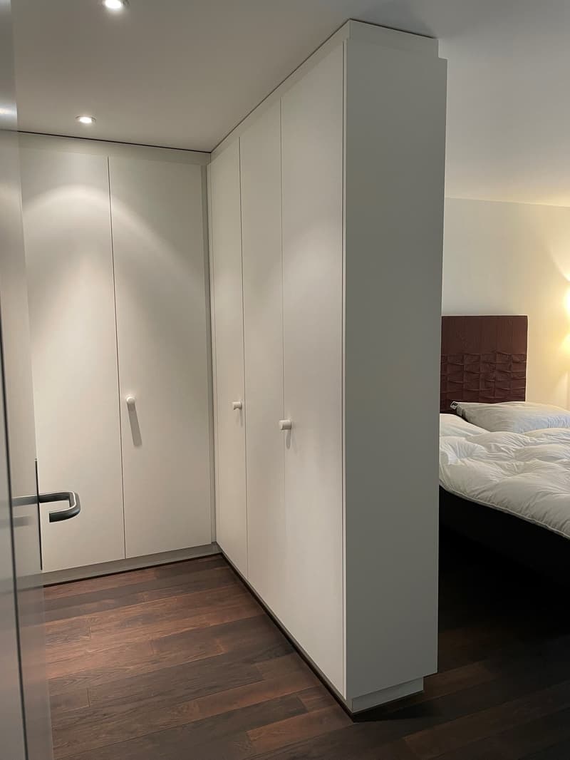 white built-in closets, bed with white bedding, wooden floor