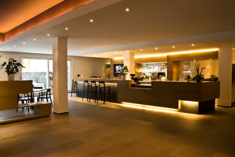 Large open space with a bar and seating area, warm lighting, wooden floors, and modern decor.