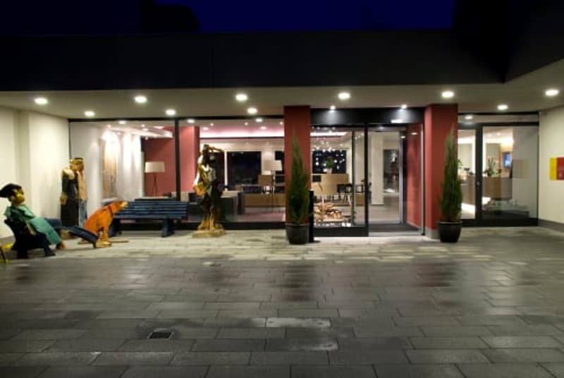 Spacious hotel lobby with modern decor, including large windows, potted plants, and a seating area. The lobby appears to have a reception desk and other amenities typical of a hotel entrance.