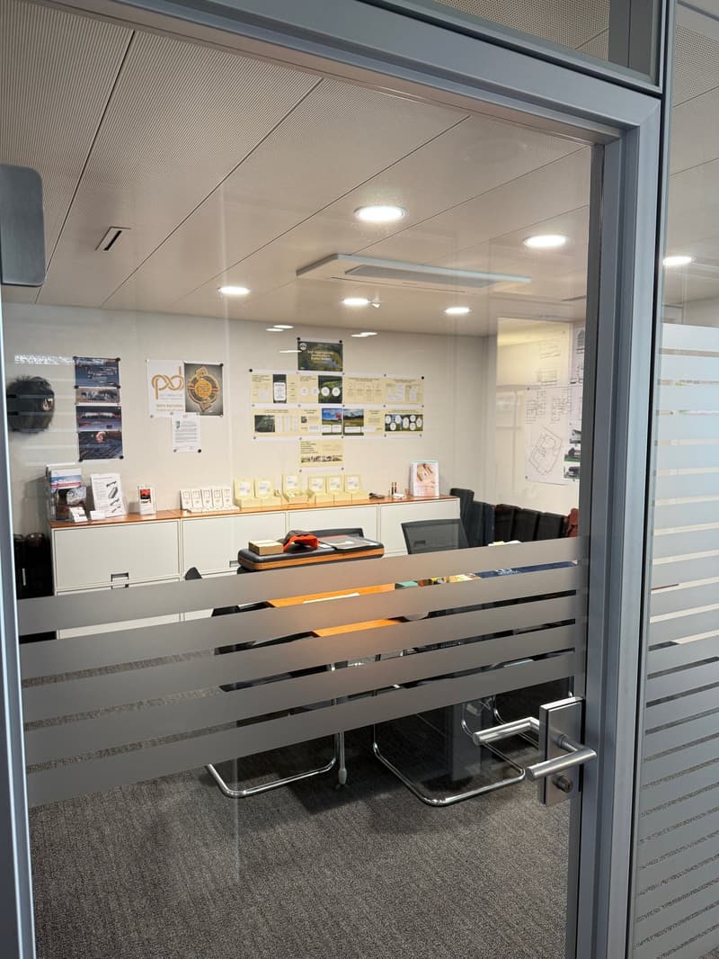modern office with glass door, white walls, gray carpet, desks, chairs, cabinets, posters, ceiling lights