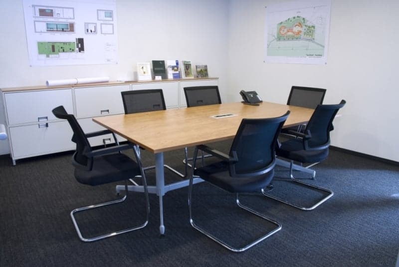 empty meeting room with a long table, 6 chairs, a telephone, and a cabinet with books