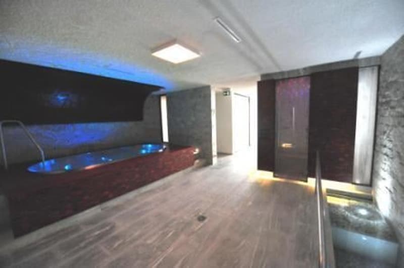 A room with a large wooden bathtub, blue lights, wooden floor, and a glass door.