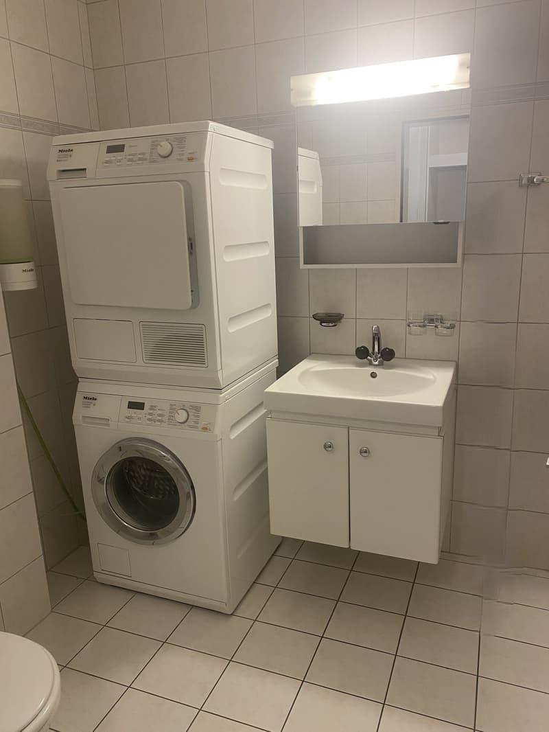 white tiled walls and floor, mounted washing machine and dryer, vanity with sink and mirror, separate toilet