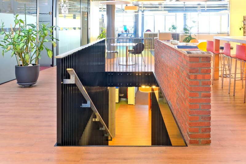 Open office layout with a raised ground floor, wooden flooring, brick wall, and potted plants