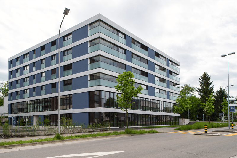 6-storey blue building, windows with black frames, outdoor plants, empty parking space