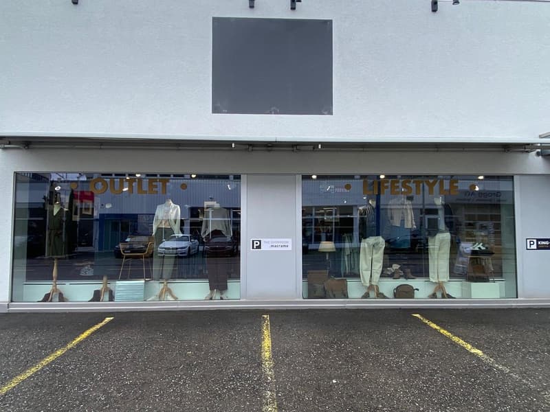 Storefront with glass windows and parking area in front, mannequins and displayed clothes inside