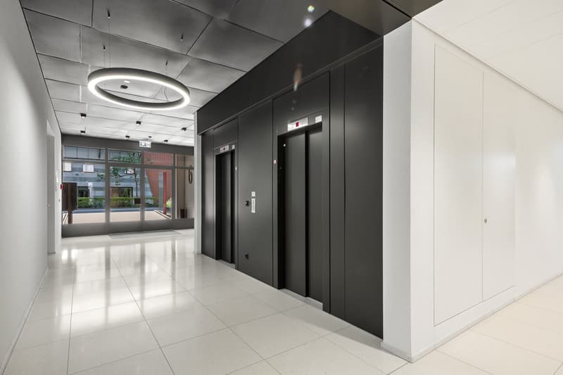 Empty entrance with clean white tile flooring, black elevator walls, glass entrance doors, and round ceiling light fixture