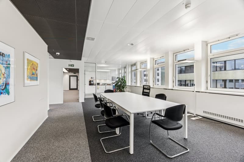 modern meeting room, white desk, black chairs, gray floor, windows, paintings