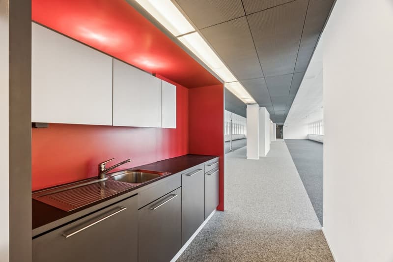 Empty kitchen with red wall, stainless steel sink, silver countertop, silver cabinet drawers and silver faucet