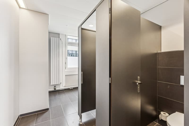 a clean, minimalist bathroom with a toilet, two cubicles, and tiled floors.