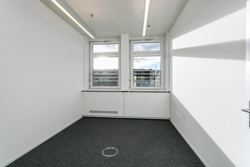Empty room with white walls, ceiling, and grey floor, two windows, and built-in cabinets