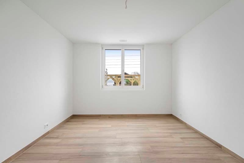 Empty room with white walls, wooden floor, a large window overlooking outside.