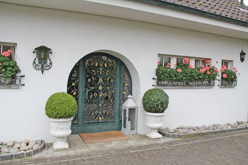 white house, green door, window boxes with flowers, two white topiary bushes, lantern, doormat