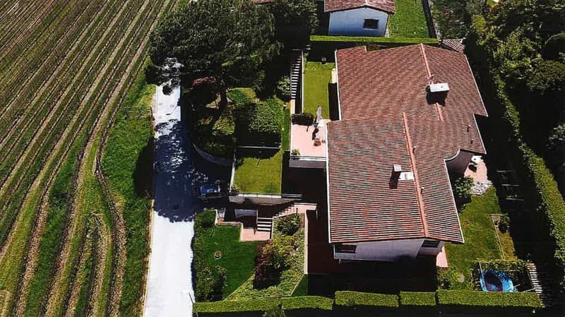 2-story house with red tile roof, surrounded by lush greenery and a stream, with a garage and parking space visible