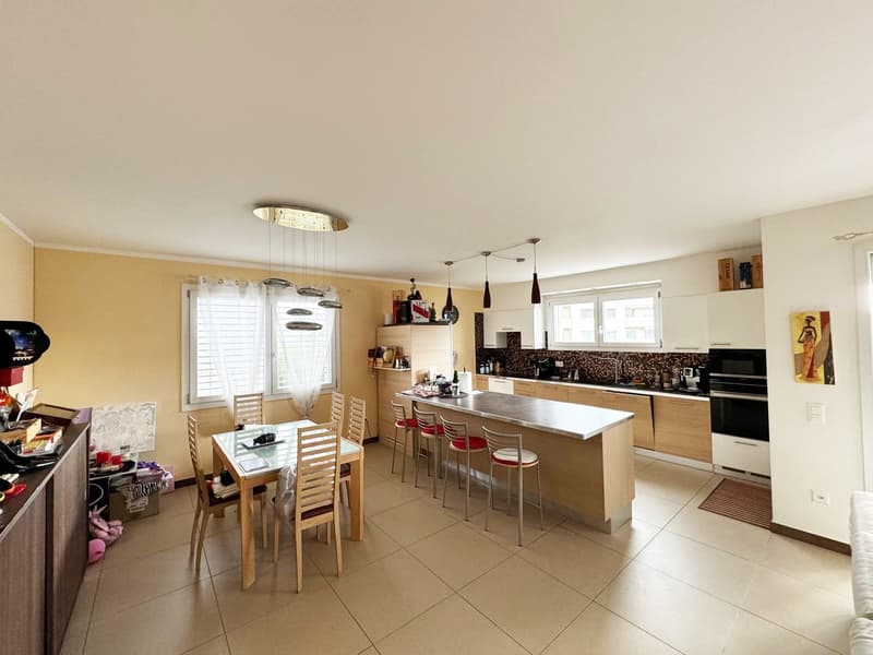 Spacious open-concept kitchen with wooden cabinets, black and white tile backsplash, island with bar stools, dining table, and appliances including a dishwasher