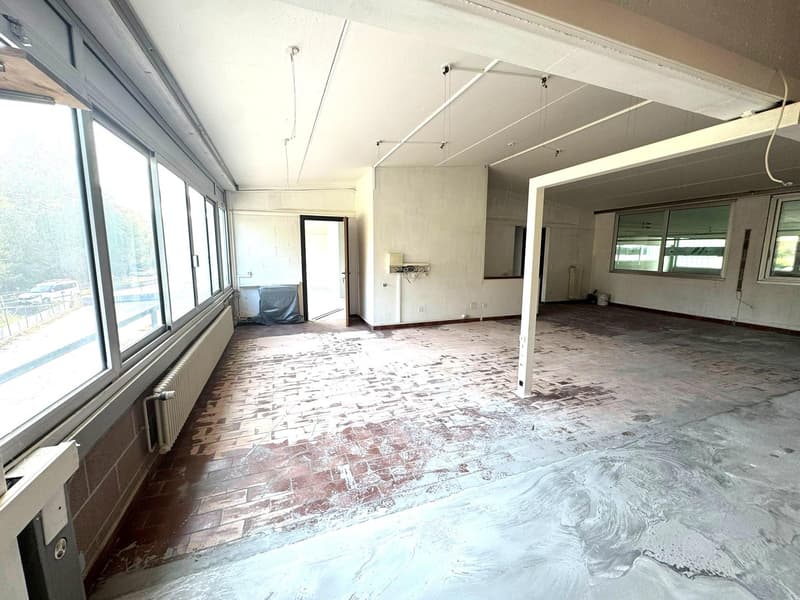 Empty room, large windows, concrete floor, white walls, brick floor, exposed pipes