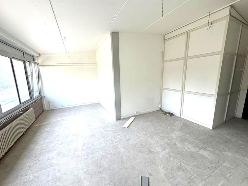 Empty room with white walls, concrete floor, a window, a white radiator, electrical outlet on wall