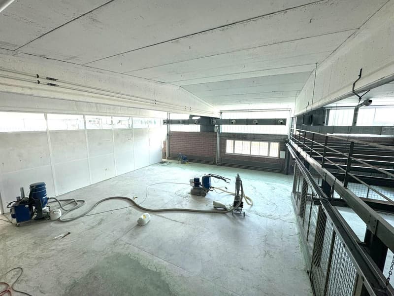 empty, concrete floor, white walls, machinery on floor, multiple windows, metal railings on one side