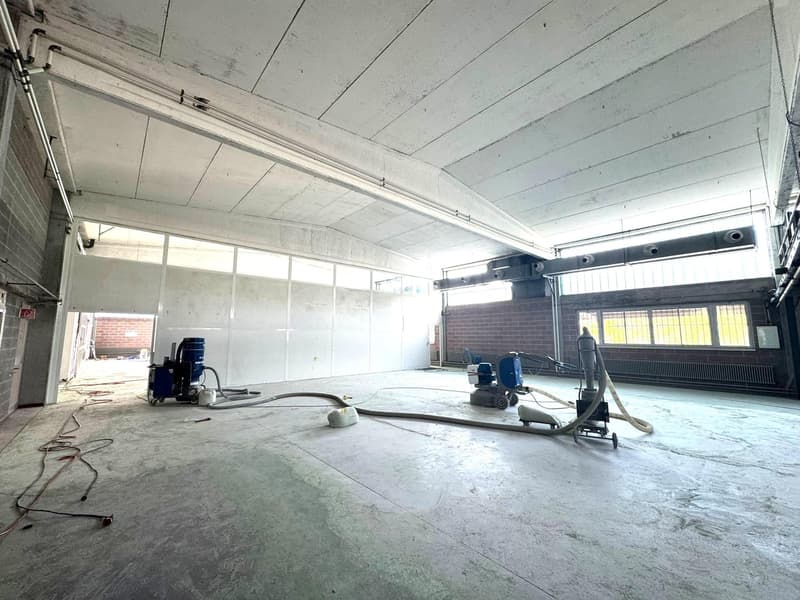 Concrete floor, white ceiling, industrial machines, large windows, open doorway