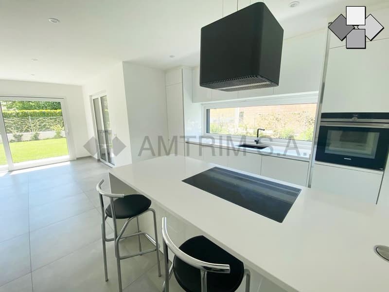 Modern, open-concept kitchen with white cabinets, black countertops, built-in dishwasher, and large windows overlooking the backyard.