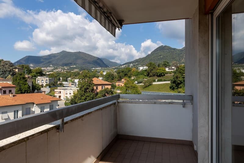 Balcony with metal railing, tiled floor, view of mountains and buildings