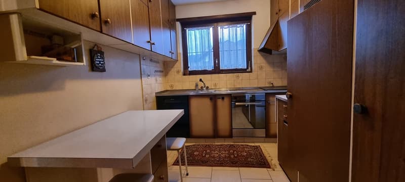 small kitchen, tiled floor, wooden cabinets, sink, dishwasher, countertop, window with curtain, rug, stool