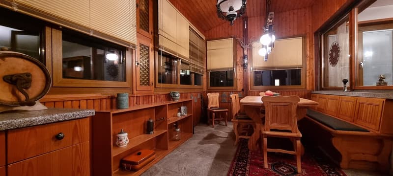 a dining area with wooden table, wooden chairs, wall with windows, a wooden bench, wooden cupboards and lamps